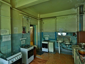 газовые плиты, раковины и рабочие столы у стен с голубой плиткой в кухне коммунального общежития