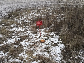 геомаркер на открытом поле с засохшей травой под снегом у небольшой деревни