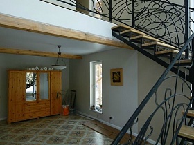 четырехдверный деревянный шкаф с зеркалами в светлой зоне гостиной под лестницей с кованными черными перилами недостроенного элитного дома