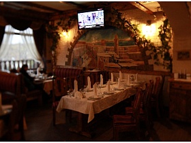 красочно оформленная центральная стена с красивой арочной картиной, обвитой виноградной лозой, телевизором и теплыми бра в уютном зале ресторана с кавказким интерьером
