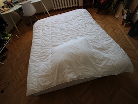 кровать с подушкой под белым стеганным покрывалом на паркетном полу современной комнаты в трехкомнатной квартире