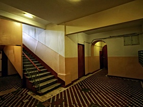 мелкая коричнево белая плитка на полу в холле первого этажа с кремовым панелями и белым потолком сталинского здания с полисадником и пандусом