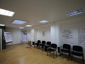 просторная рабочая комната с белыми стенами и белым потолком, мягкими черными стульями вдоль стены