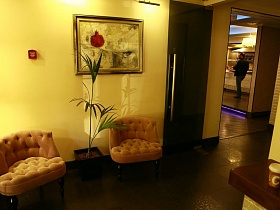 мягкие персиковые кресла , высокая пальма в квадратном вазоне у желтой стены с большой картиной в рамке в холле интересного ресторана на Юге Москвы