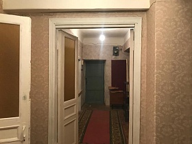 черный электросчетчик, деревянная настенная вешалка для одежды на стене у входной серой двери прихожей с красной дорожкой на полу квартиры N6