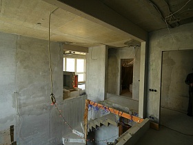 общий вид второго этажа с бетонной витой лестницей и открытыми дверными проемами в различные комнаты просторной квартиры молодежи без ремонта