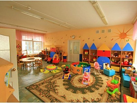 детские коляски, машинки, мячи,имитация домиков с игрушками, круглым столом в младшей группе с солнышком на персиковой стене