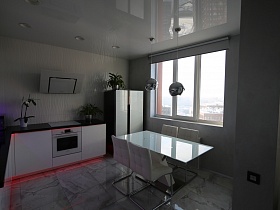 белые стулья со спинкой на металлических ножках вокруг стола со стеклянной поверхностью у большого окна кухни в серых тонах