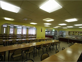 ряды из нескольких столов и стульев напротив витрины и линии раздачи питания в красивой столовой современной школы