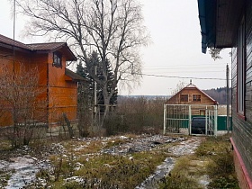 машина за высоким белыми металлическими воротами сетчатого забора в конце участка с деревянным домиком в деревне