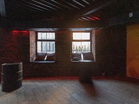 металлические круглые бочки на деревянном полу у окон с подушками на подоконнике в кирпичной стене ночного клуба лофт