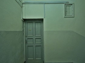 серые деревянные двери жилой квартиры в подъезде с серыми стенами и панелями в доме советского времени