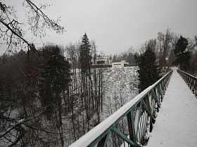 пешеходный подвесной мост в зимнее время над протекающей речкой и густым лесом на побережье