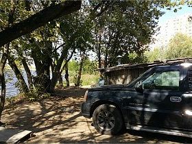 черная машина в тени деревьев на берегу реки