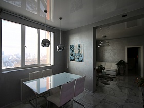 две подвесные люстры с зеркальными плафонами над обеденным стеклянным столом у большого окна кухни в стиле минимализм