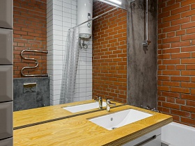 стиральная машинка под деревянной столешницей с белой раковиной,большое прямоугольное зеркало с лампой дневного света у бетонной стены в ванной комнате стильной студии лофт