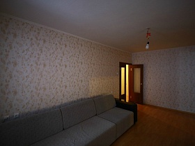 большой светлый угловой мягкий диван с подушками и черными подлокотниками у стены с цветными обоями гостиной большой трехкомнатной квартиры в переезде