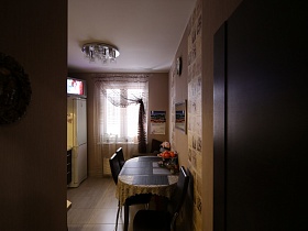 овальный обеденный стол и стулья у стены, белый холодильник на светлом полу кухни из открытой двери современной модной квартиры в Измайлово