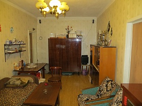 общий вид гостиной комнаты со светлыми полосатыми обоями на стенах и желтыми плафонами подвесной люстры на белом потолке двухкомнатной квартиры молодой советской семьи