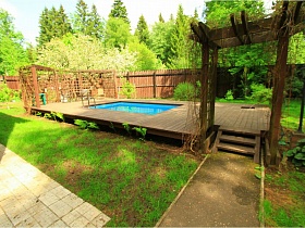 бассейн с чистой голубой водой на деревянной площадке со ступенями во дворе современного дома под съем