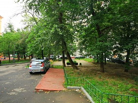 зеленый полисадник с многочисленными деревьями у сталинского здания с пандусом