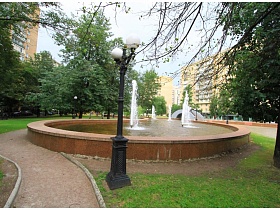 круглый фонтан среди зеленых деревьев в парке жилого квартала