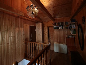 полки с книгами на стене, зеркало над столиком на деревянной лестничной площадке с люстрой в потолке над лестницей современной семейной дачи