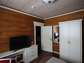 зеркало в белой рамке и белый шкаф для одежды в спальне деревянного съемного коттеджа