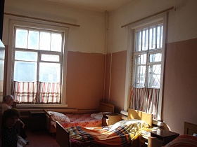 деревянные кровати с прикроватными тумбочками у стен светлой палаты с розовыми панелями, простыми ситцевыми шторками на высоких окнах старой действующей больницы