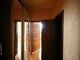 трехдверный шкаф с зеркалами в небольшом коридоре перед спальной комнатой в современной трехкомнатной квартире жилого дома