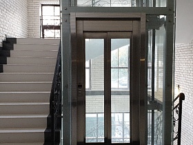 раздвижные стекляные двери стеклянного лифта в стиле хай тек в современном подъезде жилого дома
