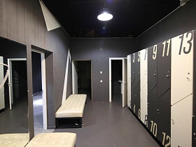 открытые двери в душевые комнаты из черной раздевалки с белыми банкетками и белыми геометрическими фигурами на стене