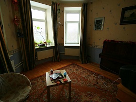 полукруглое светлое кресло, альбомы и тетради на деревянном детском столике на цветном коричневом ковре на полу гостиной семейной трехкомнатной квартиры