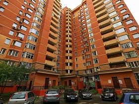 современное многоэтажное красивое жилое двухцветное здание в бежево-коричневом цвете с припаркованными машинами во дворе