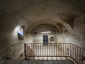 Темница, серые бетонные стены, оконце, лестница со ступеньками в подполье