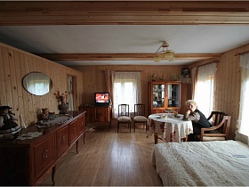 круглый стол, шкаф для посуды и телевизор на тумбочке в большой гостинной деревянной дачи у дороги