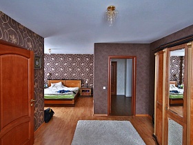 светлый ковер на полу и большая кровать с подушкой у коричневой стены с цветами и вензелями спальной комнаты современного деревянного дома