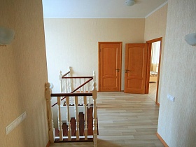 бра на бежевых стенах холла второго этажа с лестницей и открытыми дверьми в комнаты кирпичного двухэтажного дома