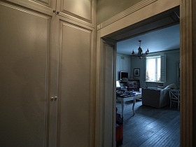 шкаф для одежды с антресолью в бежевой прихожей у открытой двери в гостиную современной дизайнерской двухкомнатной квартиры