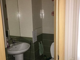 высокое прямоугольное зеркало над небольшой белой раковиной, санузел в туалетной комнате с двухцветной плиткой на стене