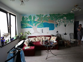 две люстры на белом потолке гостиной с разрисованной стеной в простой семейной трехкомнатной квартире