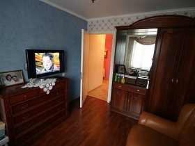 фотография в рамке, белая салфетка, телевизор на комоде и коричневый шкаф с зеркалом в гостиной современной трешки