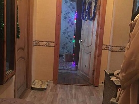 коричневая прихожая с одеждой на крючках, прямоугольное зеркало на стене прихожей с открытой дверью в спальную комнату квартиры СССР