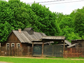 деревянный бревенчатый домик с белыми наличниками на окнах за дощатым забором с высокими воротами в старом городке для съемок кино