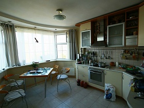 светлая мебель с газовой плитой, мойкой и многочисленными шкафчиками в просторной кухне трехкомнатной квартиры многоэтажки