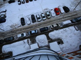 вид из окна квартиры в Новострое на автомобильную дорогу вдоль высотного здания с припаркованными машинами