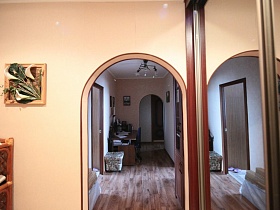 обувная полка и шкаф-купе с зеркальными дверцами у арочного дверного проема в прихожей яркой трехкомнатной квартиры с комнатой бабушки