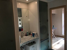 прямоугольное зеркало над раковиной в серо-белой столешнице, между встроенными шкафами в ванной комнате трехкомнатной квартиры с дизайнерским ремонтом