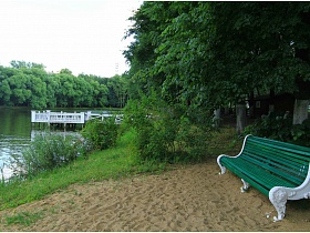 зеленая деревяенная скамейка на песчанном берегу романтического пруда