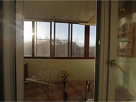 сушилка для белья, желтые подсолнухи в вазе на полу застекленного балкона простой просторной двухкомнатной квартиры